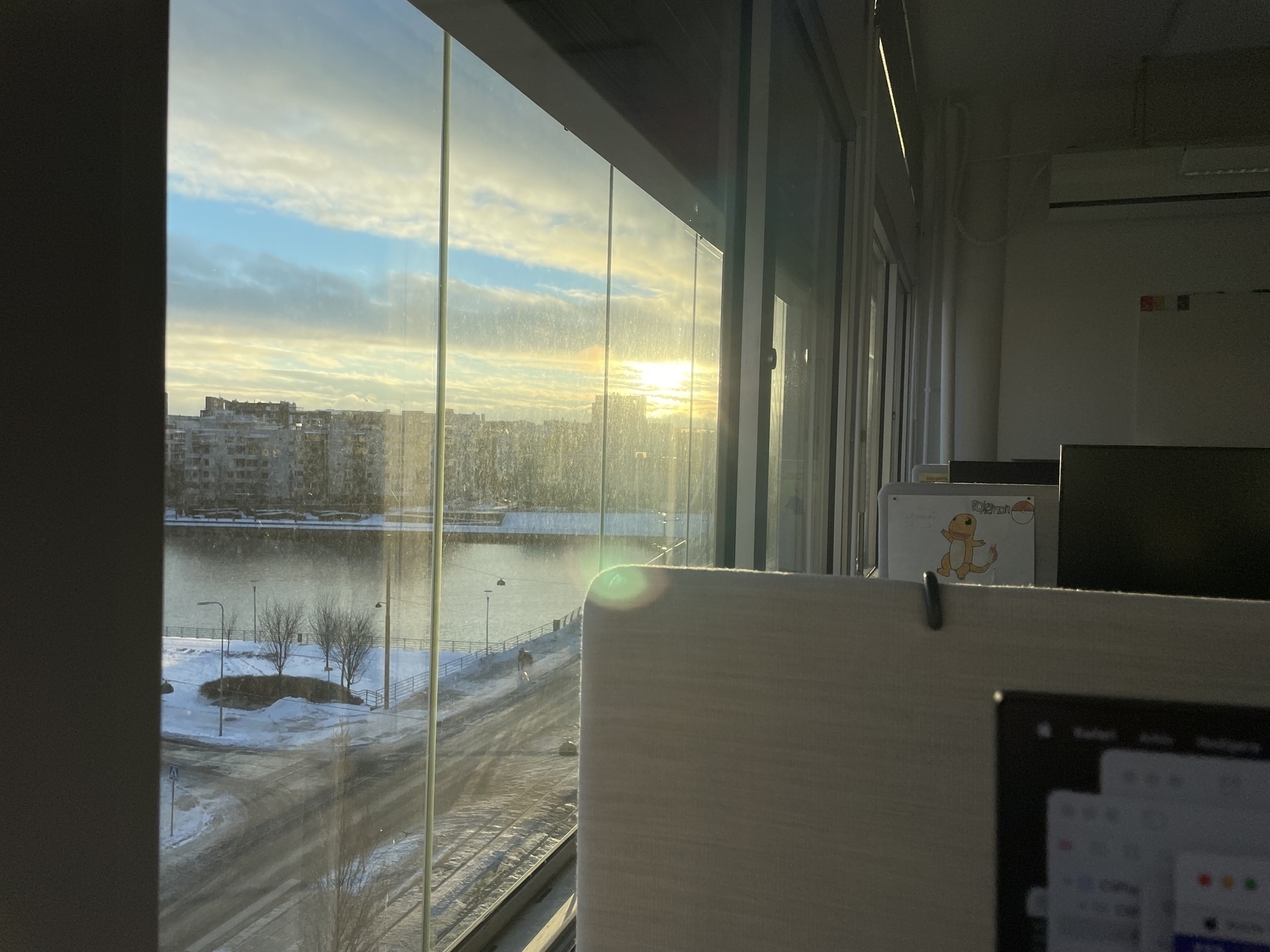 View from an office window. Sunrise over a city landscape (Jätkäsaari, Helsinki). There is a canal crossing the view and snow on the ground. 